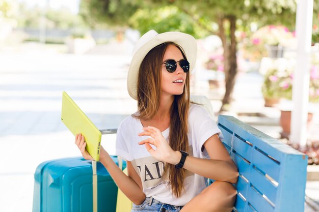 Jolie fille assise sur un banc bleu et jouant sur une tablette dans un étui jaune.