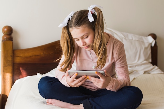 Jolie fille assise sur le lit regardant smartphone