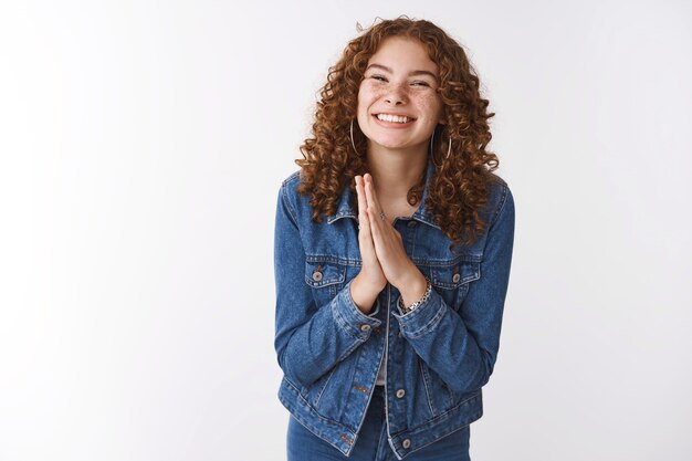 Jolie fille aux taches de rousseur rousse charmante et pleine d'énergie portant des paumes de presse en denim ensemble fait un sourire d'ange le regard implorant la faveur de la main priez, dites s'il vous plaît prêter de l'argent, debout sur fond blanc