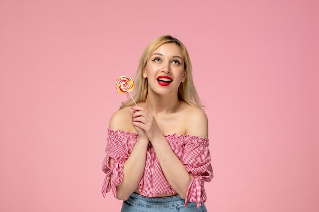 Jolie fille belle jeune femme avec du rouge à lèvres en chemisier rose tenant une sucette rose agissant mignon