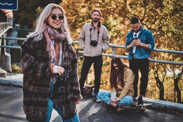 Jolie fille blonde avec appareil photo profite d'une promenade d'automne avec ses amis.