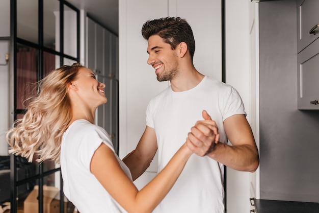 Jolie fille blonde dansant avec l'homme à la maison. Portrait intérieur de jeune femme s'amusant avec son petit ami.