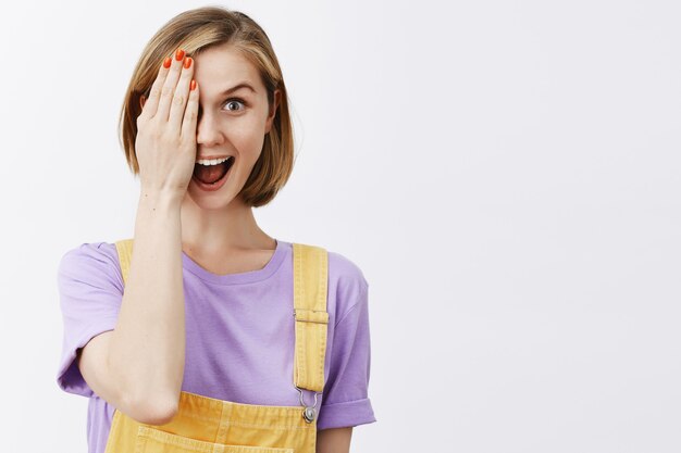 jolie fille blonde jouant peekaboo, montrant la moitié du visage et souriant amusé