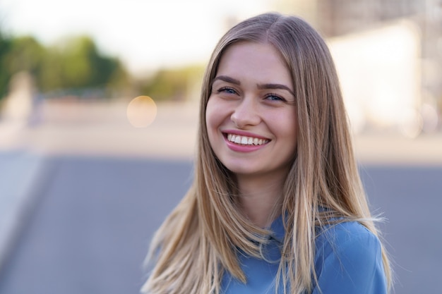 Jolie fille blonde joyeuse avec des cheveux longs volants souriant en riant dans la ville