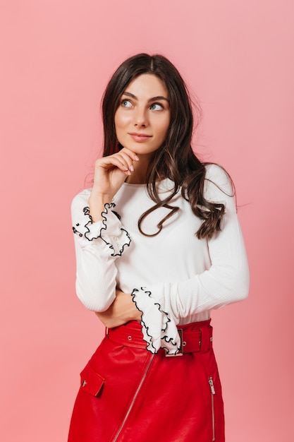 Jolie fille brune bouclée avec un léger sourire pose pour portrait sur fond rose.