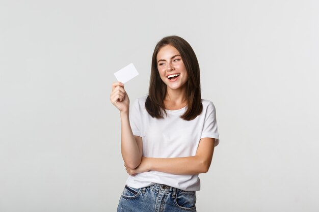 Jolie fille brune heureuse riant et tenant la carte de crédit, blanc.