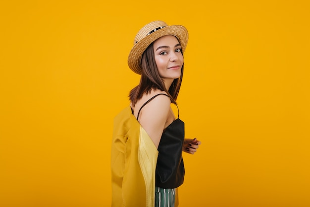 jolie fille brune porte un chapeau de paille. Portrait intérieur de magnifique dame isolée.