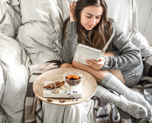 Jolie Fille Sur Une Chaise Confortable Avec Du Thé, Lisant Un Livre, Le Concept De Confort Et De Hipster