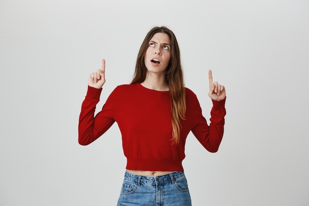 Jolie fille confuse et indécise, pointant et regardant la bannière