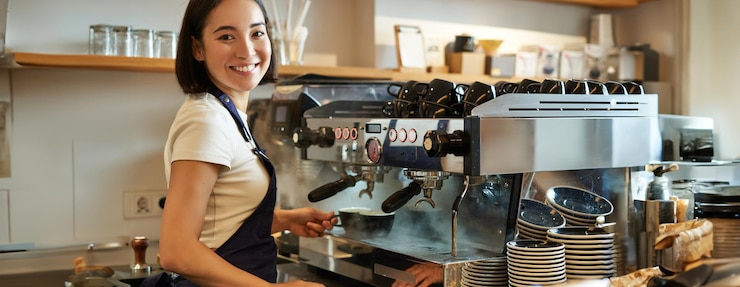 Photo gratuit une jolie fille coréenne souriante, barista travaillant avec une machine à café, prépare un cappuccino à l'aide d'un cuiseur vapeur au café