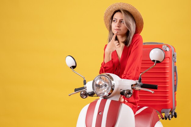 jolie fille sur cyclomoteur avec valise rouge pensant à quelque chose