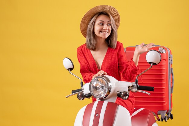 Jolie fille sur cyclomoteur avec valise rouge pointant vers la droite