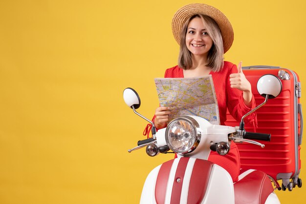 jolie fille sur un cyclomoteur avec une valise rouge tenant une carte donnant des pouces vers le haut