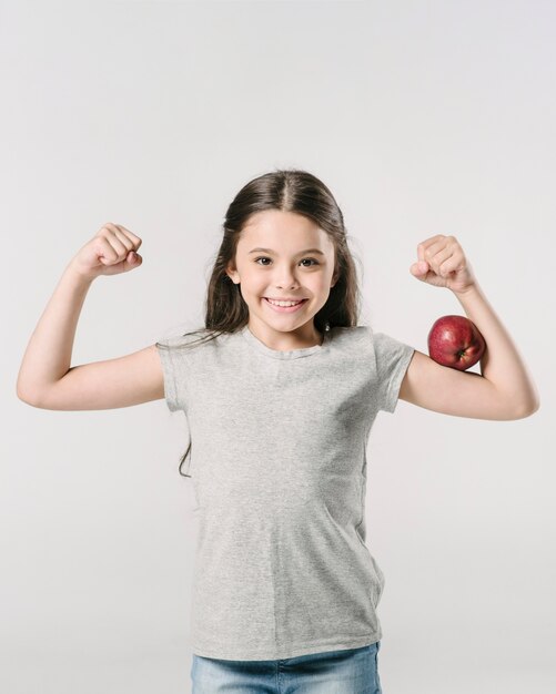 Jolie fille debout avec apple sur biceps en studio