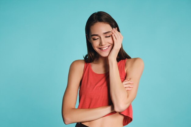 Jolie fille décontractée gaie fermant joyeusement les yeux posant sur fond coloré isolé