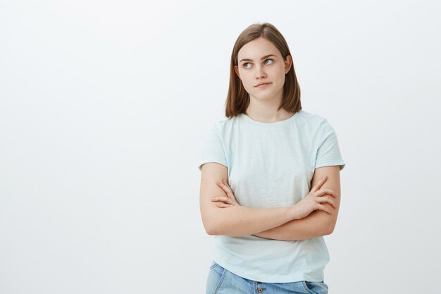 Jolie fille dérangée par un mec collant impopulaire essayant de lui demander de sortir à la gauche, irritée et ennuyée, se croisant les mains sur la poitrine et se pinçant les lèvres étant indifférent et indifférent posant sur un mur blanc