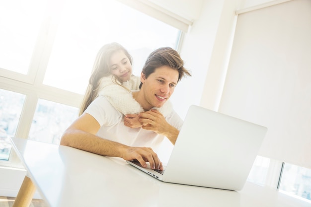 Photo gratuite jolie fille étreignant son père à l'aide d'ordinateur portable à la maison