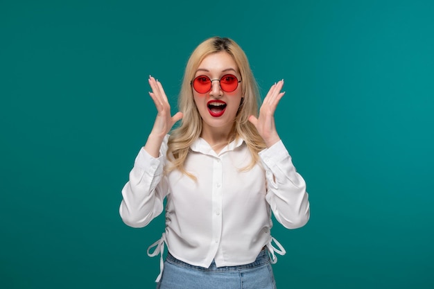 Jolie fille jeune jolie fille blonde dans une chemise blanche choquée et surprise dans des verres rouges