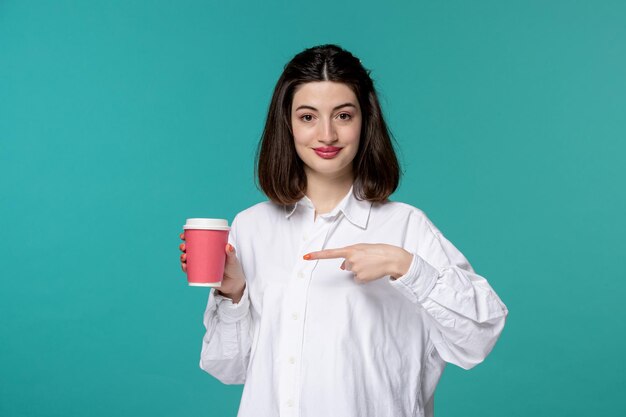 Jolie fille jolie brune jeune fille douce en chemise blanche pointant vers une tasse de café rose