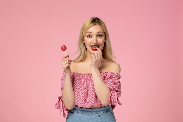 Jolie fille jolie jeune femme avec rouge à lèvres en chemisier rose mordant le doigt tenant un bonbon