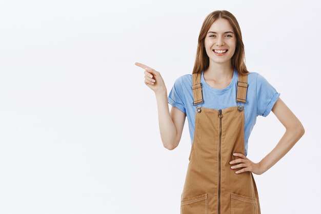 Jolie fille joyeuse pointant le doigt à gauche sur le logo, annoncer l'offre