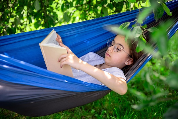 Photo gratuite jolie fille lisant un livre dans un hamac dans le jardin