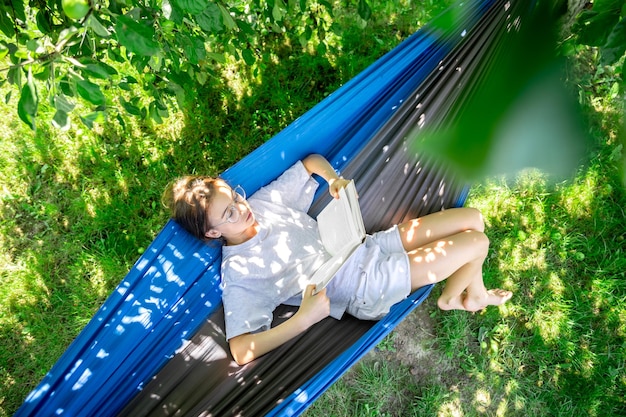 Photo gratuite jolie fille lisant un livre dans un hamac dans le jardin