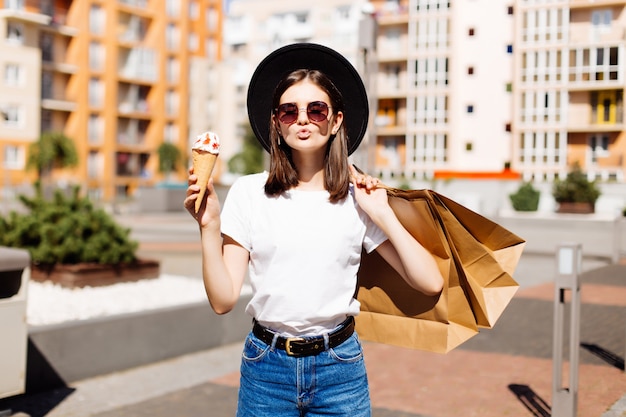 Jolie fille marchant avec de la crème glacée tenant des sacs à provisions dans un centre commercial