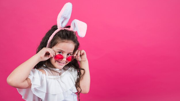 Jolie fille à oreilles de lapin ajustant des lunettes de soleil