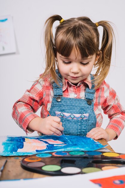 Jolie fille peignant avec la gouache bleue à la table en bois