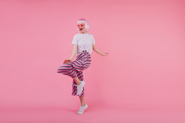 Jolie fille pleine longueur dansant dans des baskets blanches. Portrait intérieur de dame caucasienne heureuse en Pérou rose et pantalon à la mode