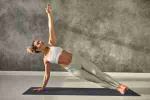 Photo gratuite jolie fille portant des leggings et haut court debout dans la planche latérale d'une part au gymnase, entraînement du corps et de l'équilibre, renforcement des muscles abs. jolie femme faisant des exercices de poids corporel de planche