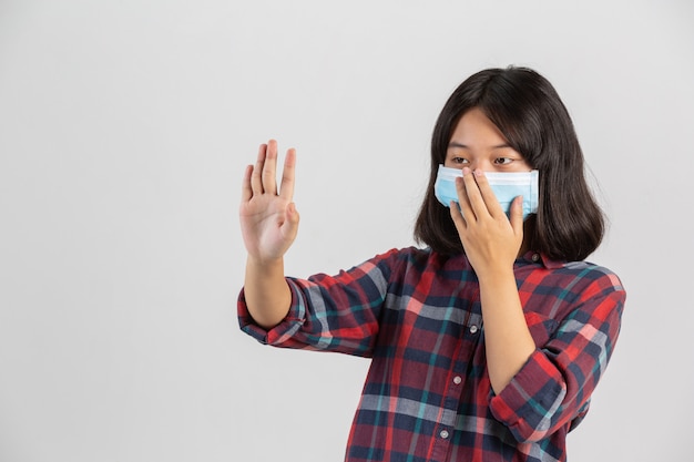 Jolie fille porte un masque et fait arrêter la main d'un autre prople sur le mur blanc.