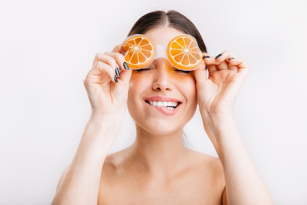 Jolie fille en prévision de l'amélioration de l'état de la peau du visage met un masque pour les yeux orange sur fond blanc