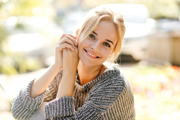 Jolie fille en pull surdimensionné à la mode se pencha et regardant la caméra sur fond de voitures avec le sourire