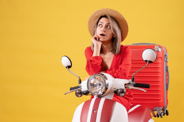 jolie fille réfléchie sur cyclomoteur avec valise rouge