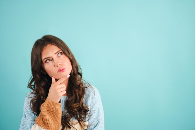 Jolie fille réfléchie en pull tricoté rêvant sur fond bleu