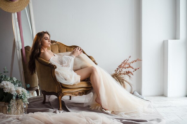 Jolie fille en robe beige avec de longs cheveux bouclés pose dans le style de mariage studio loft beaux-arts