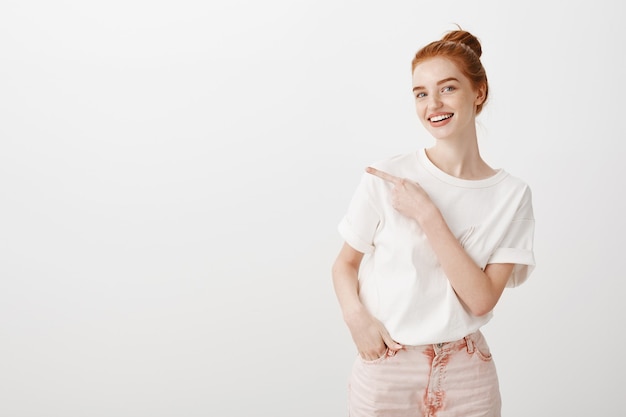 Jolie fille rousse élégante pointant le doigt à gauche et souriant