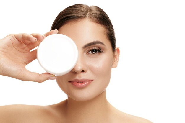 Jolie fille se prépare à commencer sa journée. Elle applique une crème hydratante sur le visage au studio. Le concept beauté, soins, peau, traitement, santé, spa, cosmétique et publicité