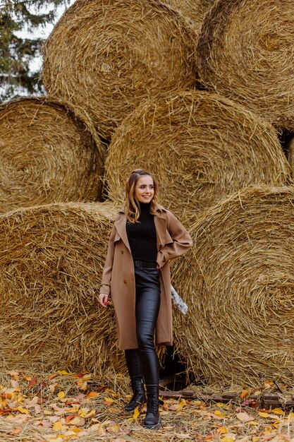 Jolie fille souriante avec chapeau posant devant des ballots de paille de blé