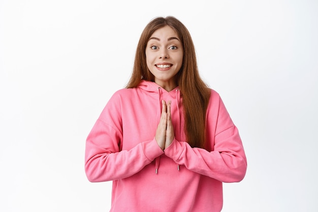 Jolie fille souriante demandant de l'aide, se tenant la main dans la prière, suppliant un geste et ayant l'air plein d'espoir, debout sur un mur blanc