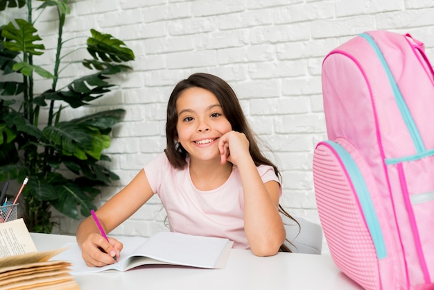 Jolie fille souriante fait ses devoirs à la maison