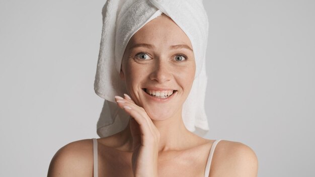 Jolie fille souriante avec une serviette sur la tête regardant joyeusement à huis clos sur fond blanc Concept de beauté