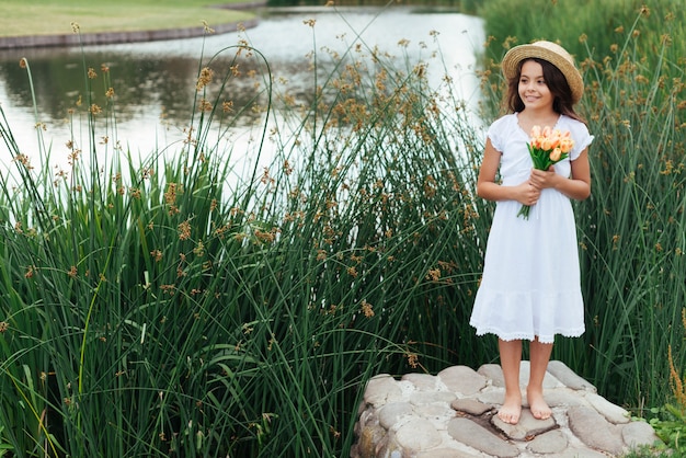 Jolie fille tenant des fleurs au bord du lac