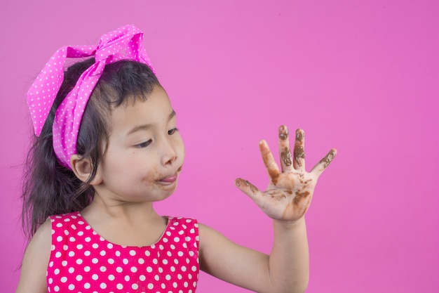 Une jolie fille vêtue d’une chemise rayée rouge mangeant un chocolat avec une bouche sale sur le rose.