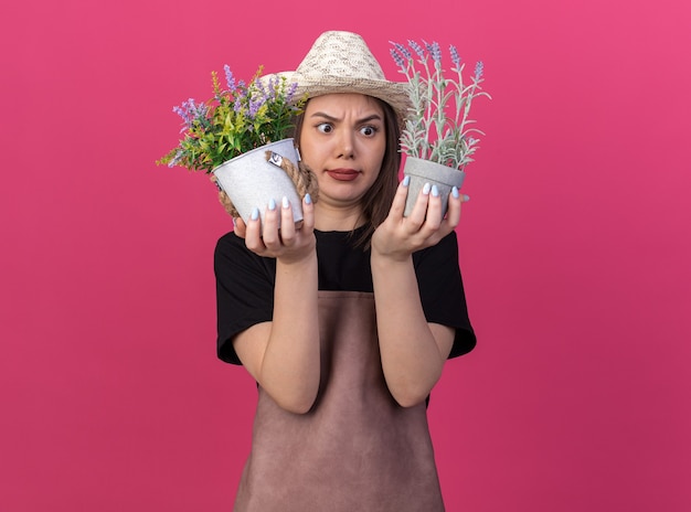 Jolie jardinière caucasienne confuse portant un chapeau de jardinage tenant des pots de fleurs