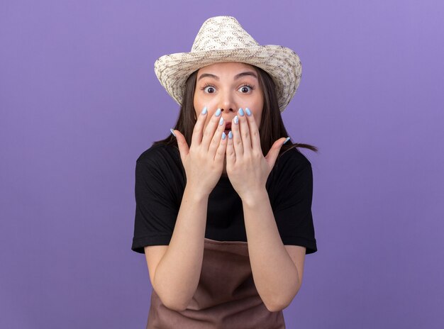 Une jolie jardinière caucasienne surprise portant un chapeau de jardinage met les mains sur la bouche