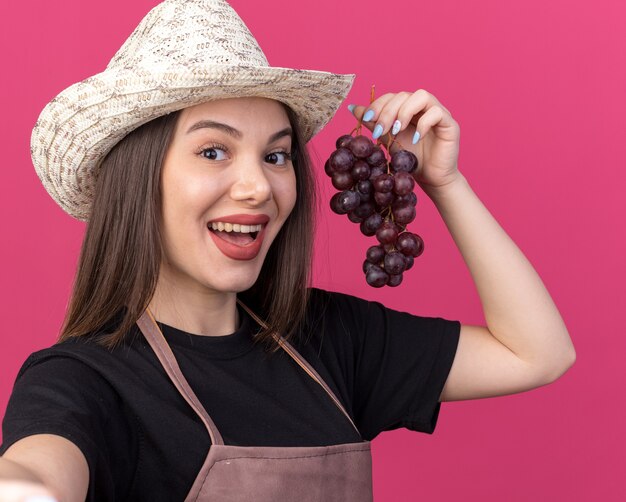 Jolie jardinière caucasienne surprise portant un chapeau de jardinage tenant une grappe de raisin