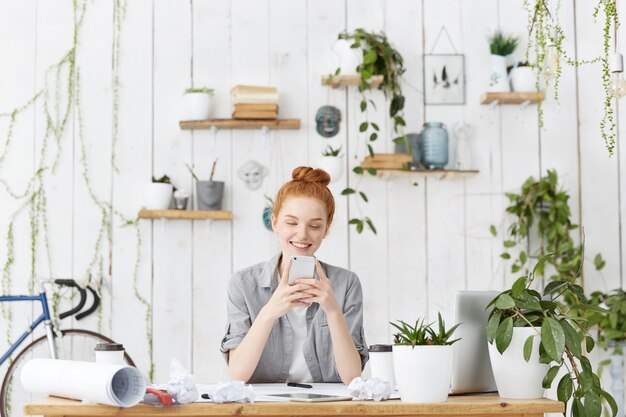 Jolie jeune architecte européenne portant ses cheveux roux en chignon assis à son espace de travail